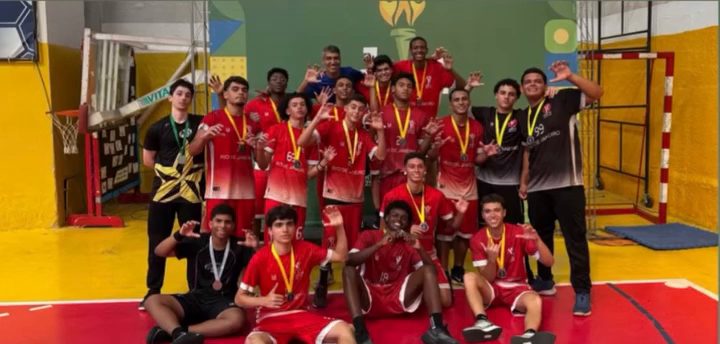 Jogadores de camisa vermelha, com medalhas no pescoço, comemoram em grupo numa quadra coberta.